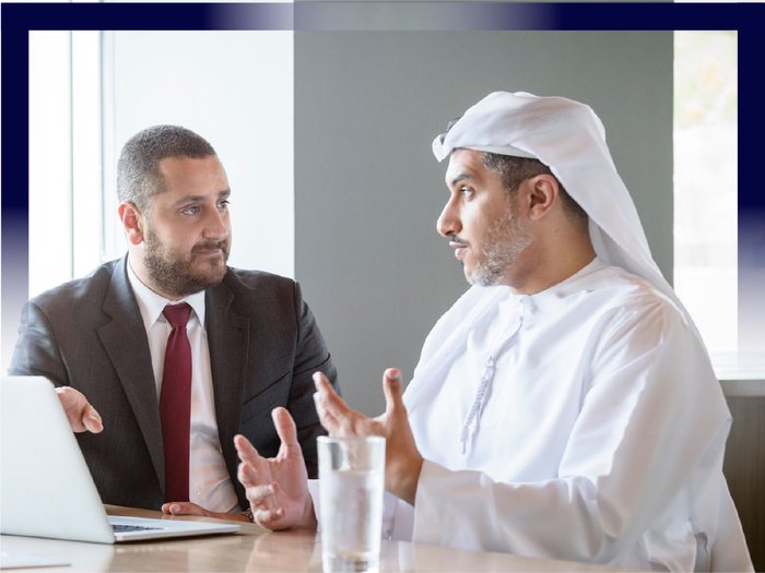 Photograph of two men in a conversation, one wearing suit and the other in traditional Middle Eastern attire.